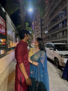 a man and woman standing next to each other in front of a building at night