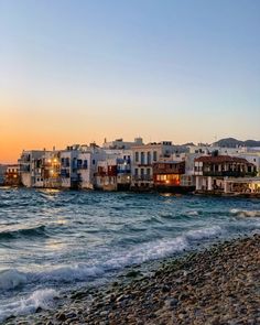 the beach is lined with white buildings and blue water at sunset in mykonos, greece