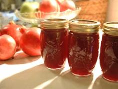 four jars filled with red liquid sitting on top of a table next to apples and other fruit