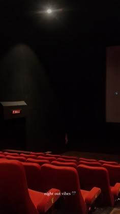 an empty theater with red seats and projector screen in the background at night time