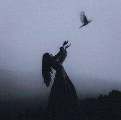 a woman standing in front of a bird flying over her head on a foggy day