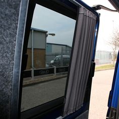 the side view mirror of a blue truck parked in front of a building with a fence