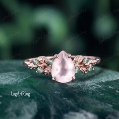 a rose quartz ring sitting on top of a leafy green surface with leaves around it