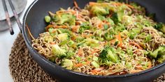 broccoli, carrots and noodles in a black bowl on a place mat