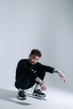 a young man kneeling down with his hand on the ground in front of him, wearing black and white sneakers