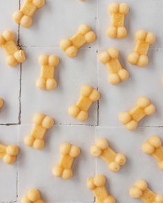 yellow dog biscuits arranged in the shape of bones on a white tile surface, top view