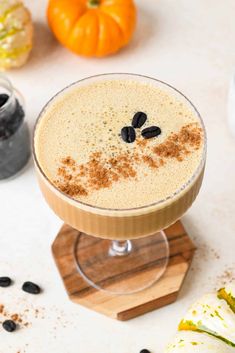 a close up of a drink in a glass on a table with pumpkins and spices