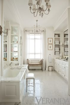 a white bathroom with a tub, sink and chandelier hanging from the ceiling