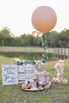 a baby sits in front of a sign and balloon