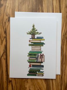 a card with a stack of books and a christmas tree on top, sitting on a wooden surface