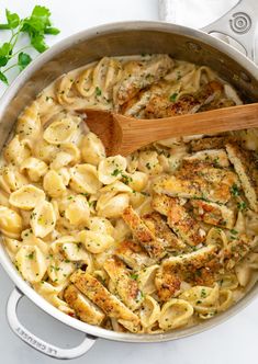 a pot filled with chicken and pasta on top of a white counter next to a wooden spoon