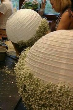 two people working on some paper lanterns in a room with flowers and other things around them