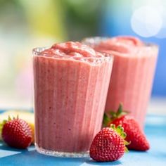 two smoothies with strawberries sit next to each other on a blue tablecloth