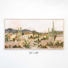 a painting hanging on the wall next to a white wall with a cactus and mountains in the background