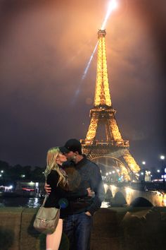 a man and woman standing in front of the eiffel tower at night with their arms around each other