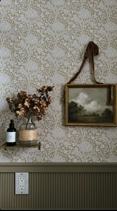 a painting hangs on the wall next to a vase with flowers in it and an old fashioned light switch