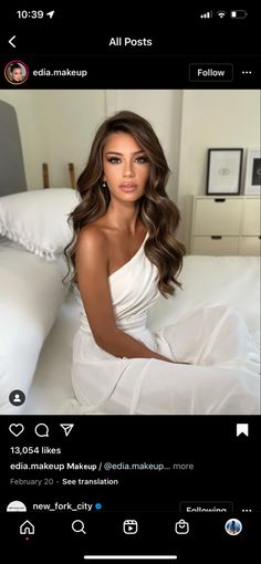 a woman sitting on top of a bed in a white dress with long brown hair