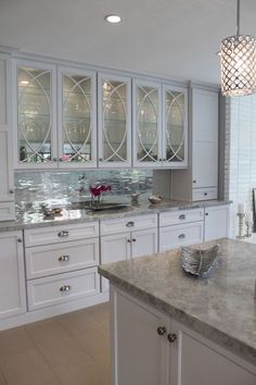 a kitchen with white cabinets and marble counter tops