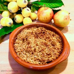 an orange bowl filled with crumbs next to green leaves and apples on a table