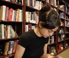 a woman is looking at her cell phone in front of a book shelf full of books