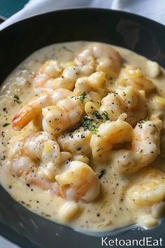 a black bowl filled with pasta and shrimp in cream sauce on top of a white table cloth