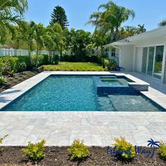 an empty swimming pool surrounded by palm trees and shrubs in front of a white house