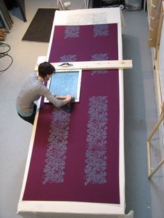 a man is working on a large piece of art in a room with purple carpet