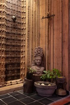 a buddha statue sitting next to a potted plant in front of a wooden door