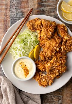 a plate with fried chicken, coleslaw and lemon wedges next to dipping sauce