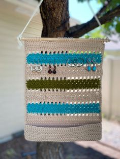 a crocheted bag hanging from a tree in front of a house with earrings on it