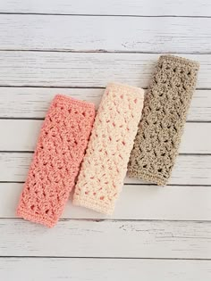 three crocheted headbands are lined up on a white wooden surface,