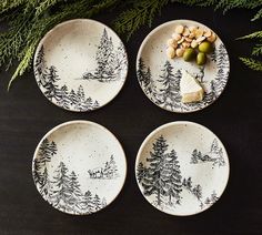 three black and white plates with pine trees on them next to evergreen branches, nuts and cheese