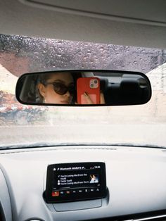 a woman taking a selfie in the rear view mirror of a car with her cell phone