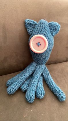 a crocheted blue stuffed animal with a button on it's head sitting on a couch