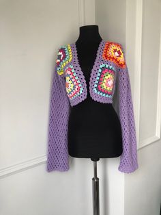 a purple crocheted jacket on a black mannequin head stand in front of a white wall