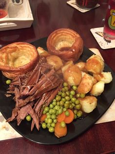 a black plate topped with meat, potatoes and veggies next to bread rolls