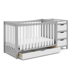 a white crib with two drawers in front of it and the bottom drawer open