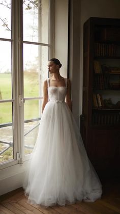 a woman standing in front of a window wearing a white dress and looking out the window