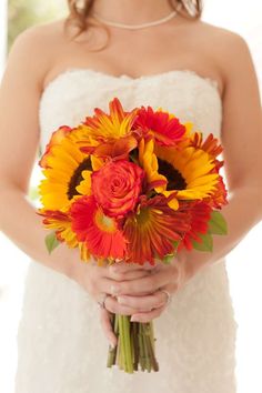 a bride holding a bouquet of sunflowers and red roses in her wedding dress