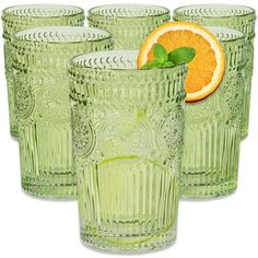 four green glass tumblers with an orange slice on the top and one in the middle