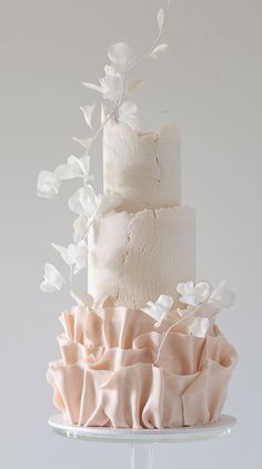 a three tiered white cake with pink ruffles and flowers on the top