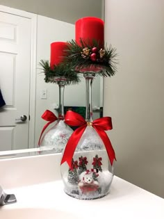 two red candles sitting on top of a white counter next to a bottle with christmas decorations