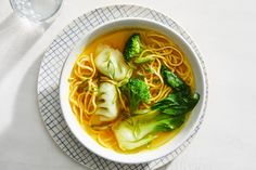 a bowl of soup with broccoli and noodles in it on a white table