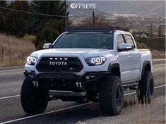 the front end of a white toyota truck driving down a road with mountains in the background