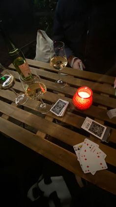 two people sitting at a table with wine glasses and playing cards on the table next to them