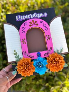 a hand holding up a pink and black photo frame with flowers on it's side