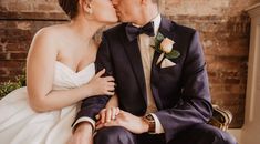 a bride and groom kissing in front of a brick wall