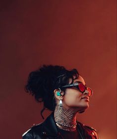 a woman with tattoos and red glasses on her face looking up at the sky while standing in front of an orange background