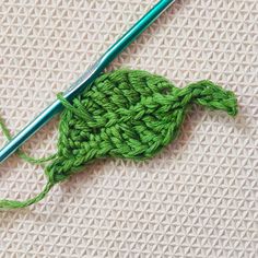 the green crochet hook is next to a knitting needle on a knitted surface