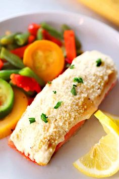 a white plate topped with fish and veggies next to a lemon wedge on top of a table